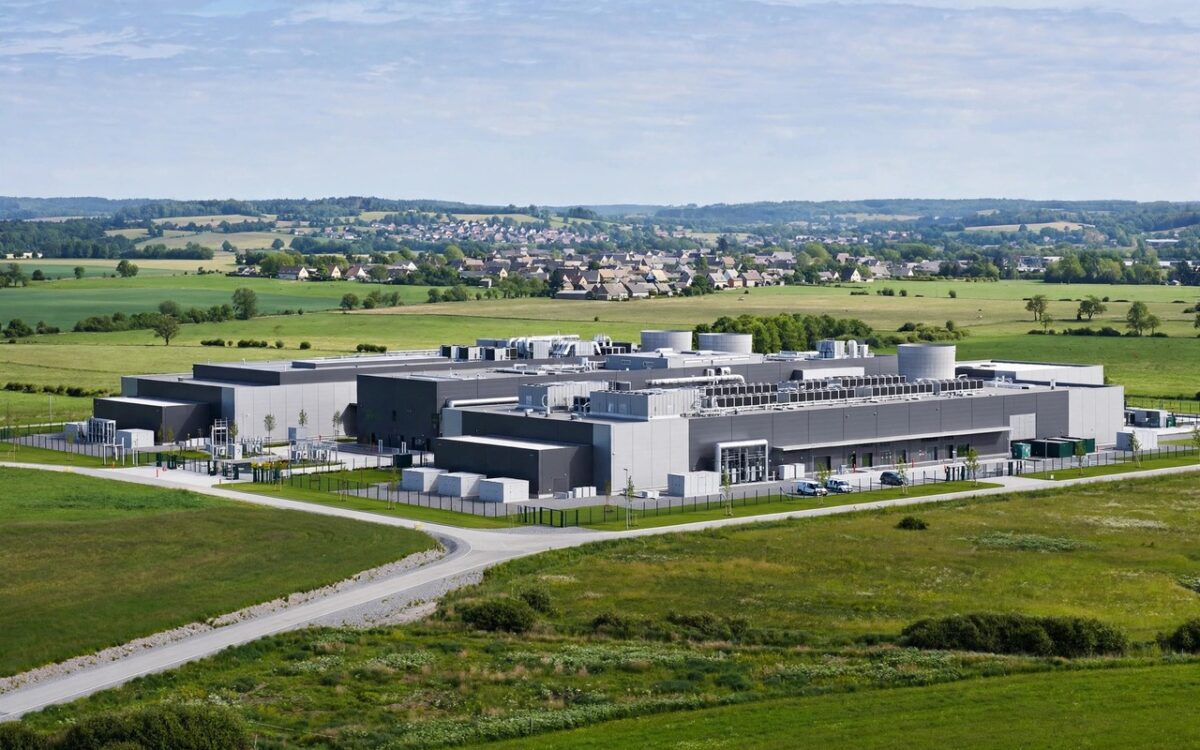 A large modern data center building on green land with small-town homes nearby