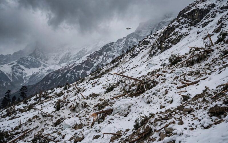 Avalanche debris on a Himalayan mountain slope with a rescue helicopter in the distance