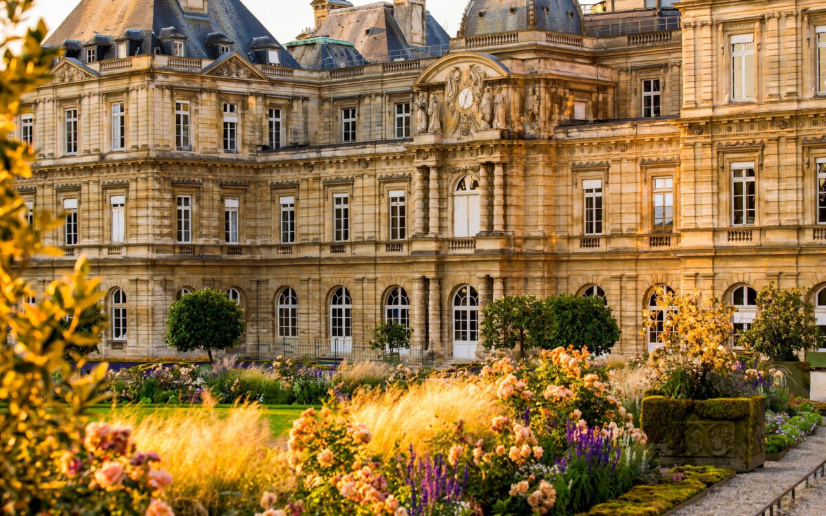The Luxembourg Palace, seat of the French Senate, glows at golden hour with its gardens in the foreground.