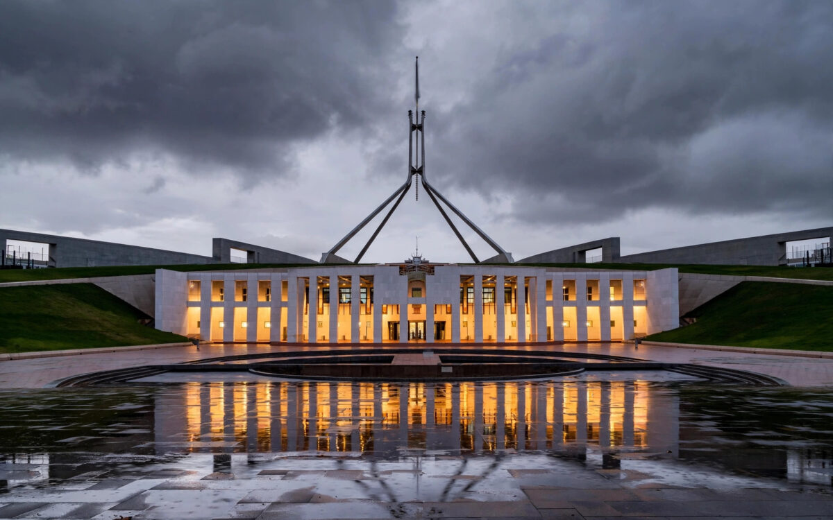Parliament House in Canberra at dusk, its tall flagpole rising above the grass-covered roof under a moody sky.