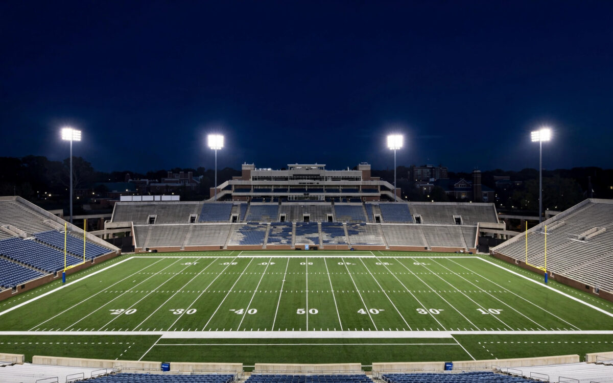 An American football stadium at night with players on the field and floodlights glowing, capturing the atmosphere of Oregon's road win over USC.
