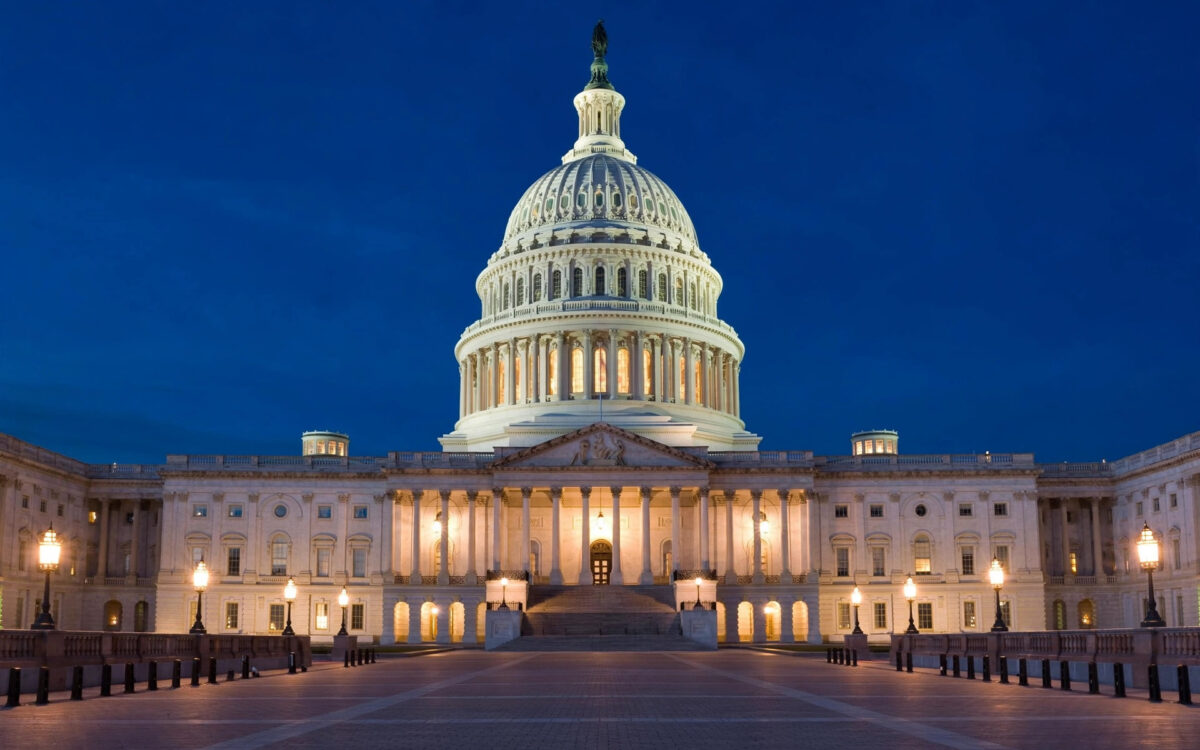 The US Capitol dome illuminated at night against a deep blue sky, plaza empty.