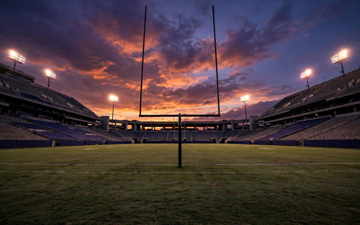 A college football end zone at dusk with a goalpost silhouetted against an orange sky.