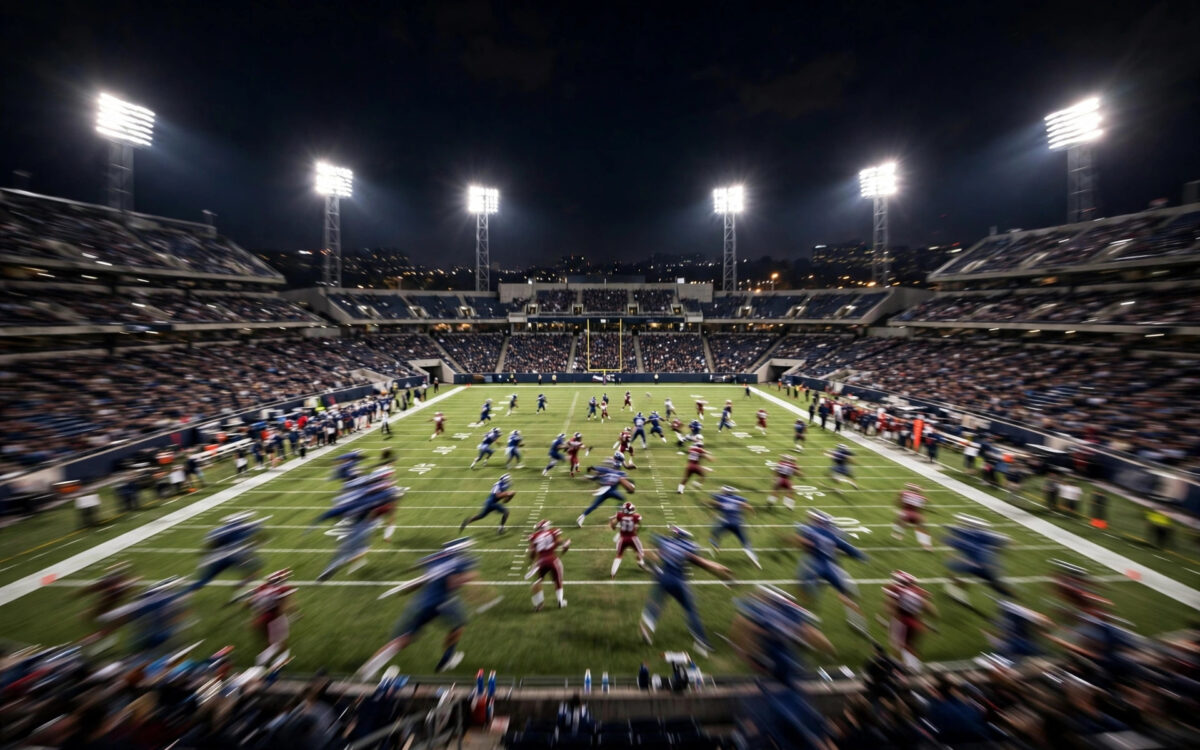 A night American football stadium with floodlights and blurred players on the green field.