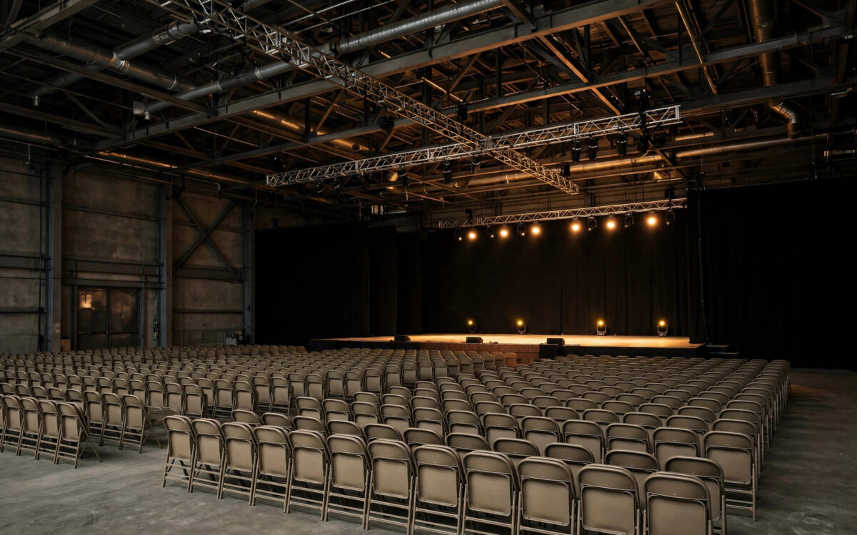 An empty indoor rally arena with rows of chairs facing a bare stage under warm spotlights.