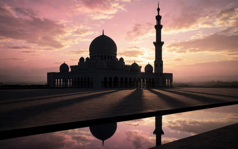 A serene mosque with dome and minaret silhouetted against a soft pink dawn sky.