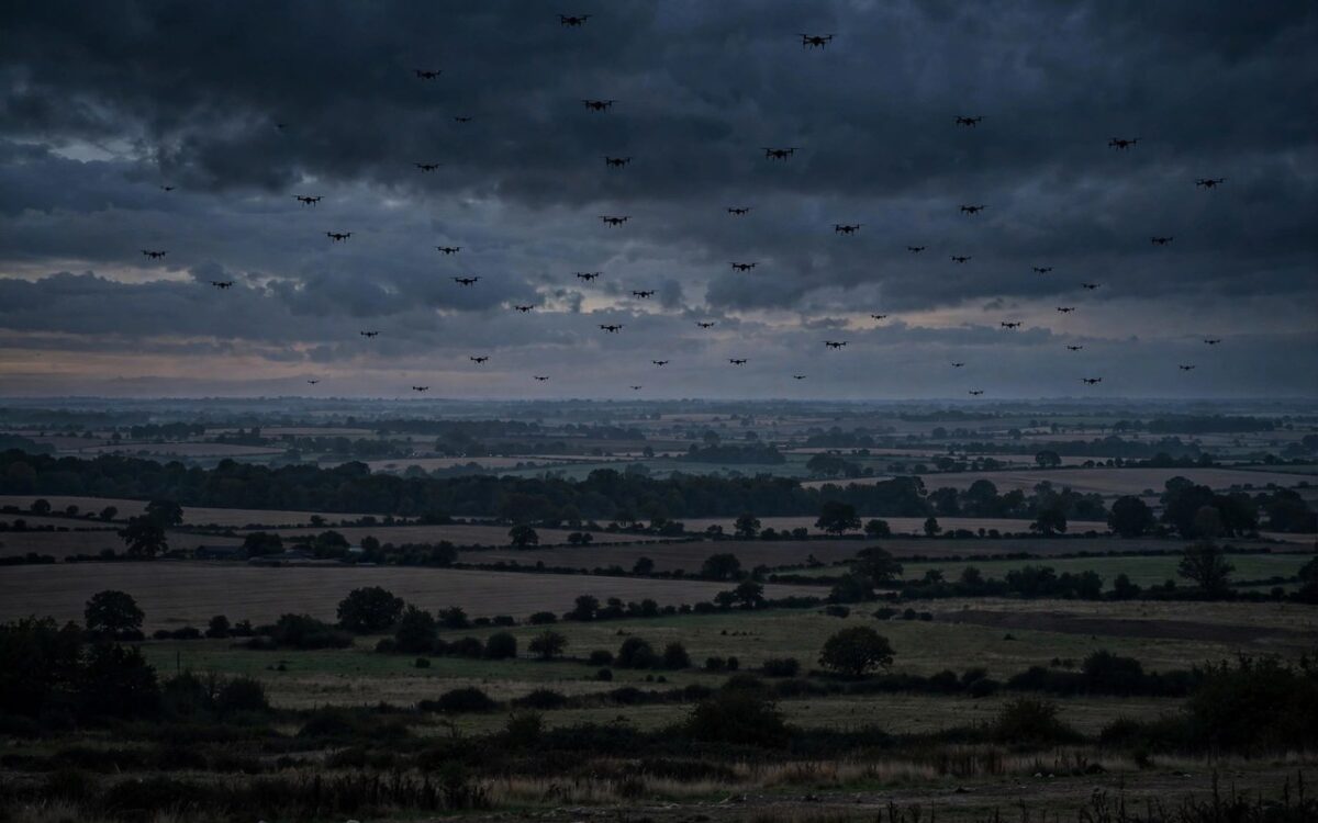 Silhouettes of drones flying over a rural landscape at dusk
