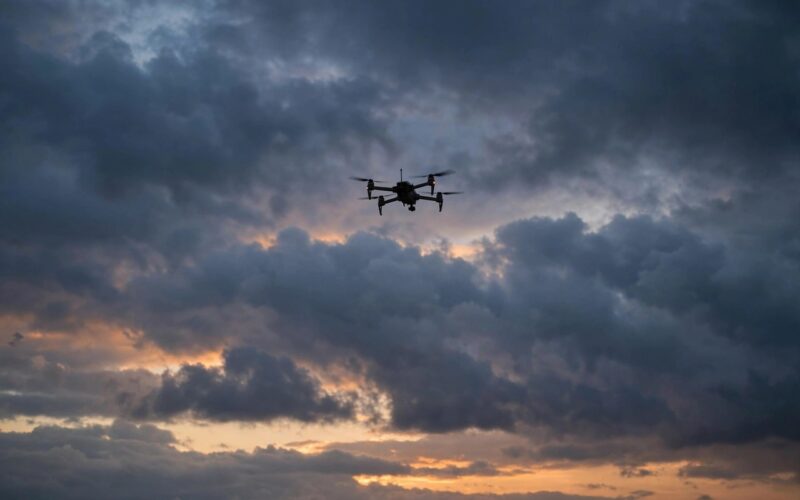 Silhouette of a military drone flying over a cloudy sky at dusk