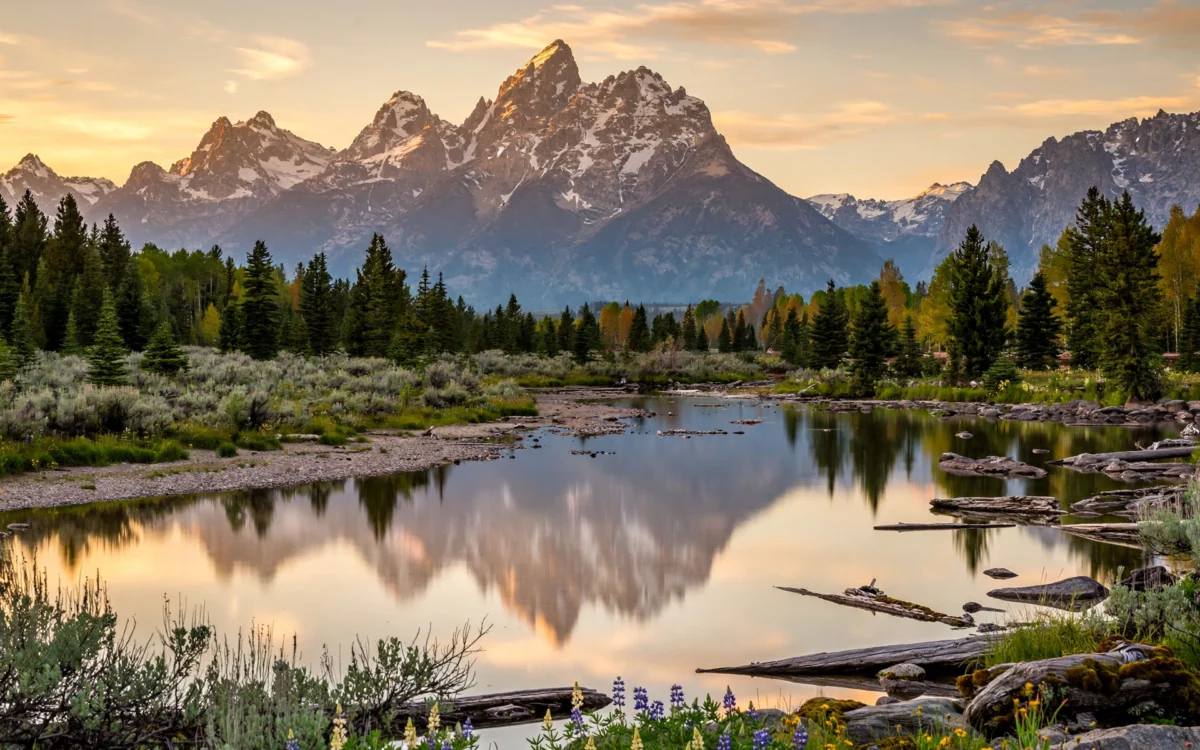 Grand Teton mountain peaks at sunrise with a lake in the foreground.