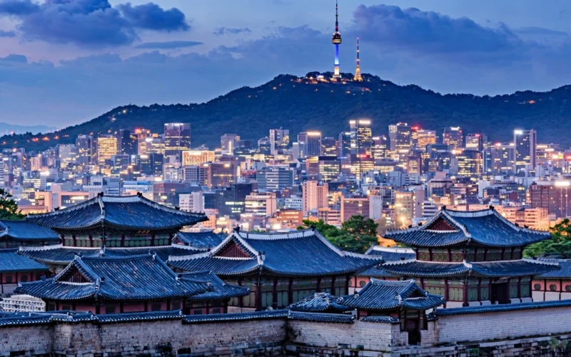 Seoul city skyline at dusk with N Seoul Tower on the mountain behind traditional palace rooftops.