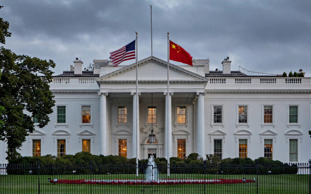 The White House stands at dusk with American and Chinese flags flying side by side under an overcast sky.